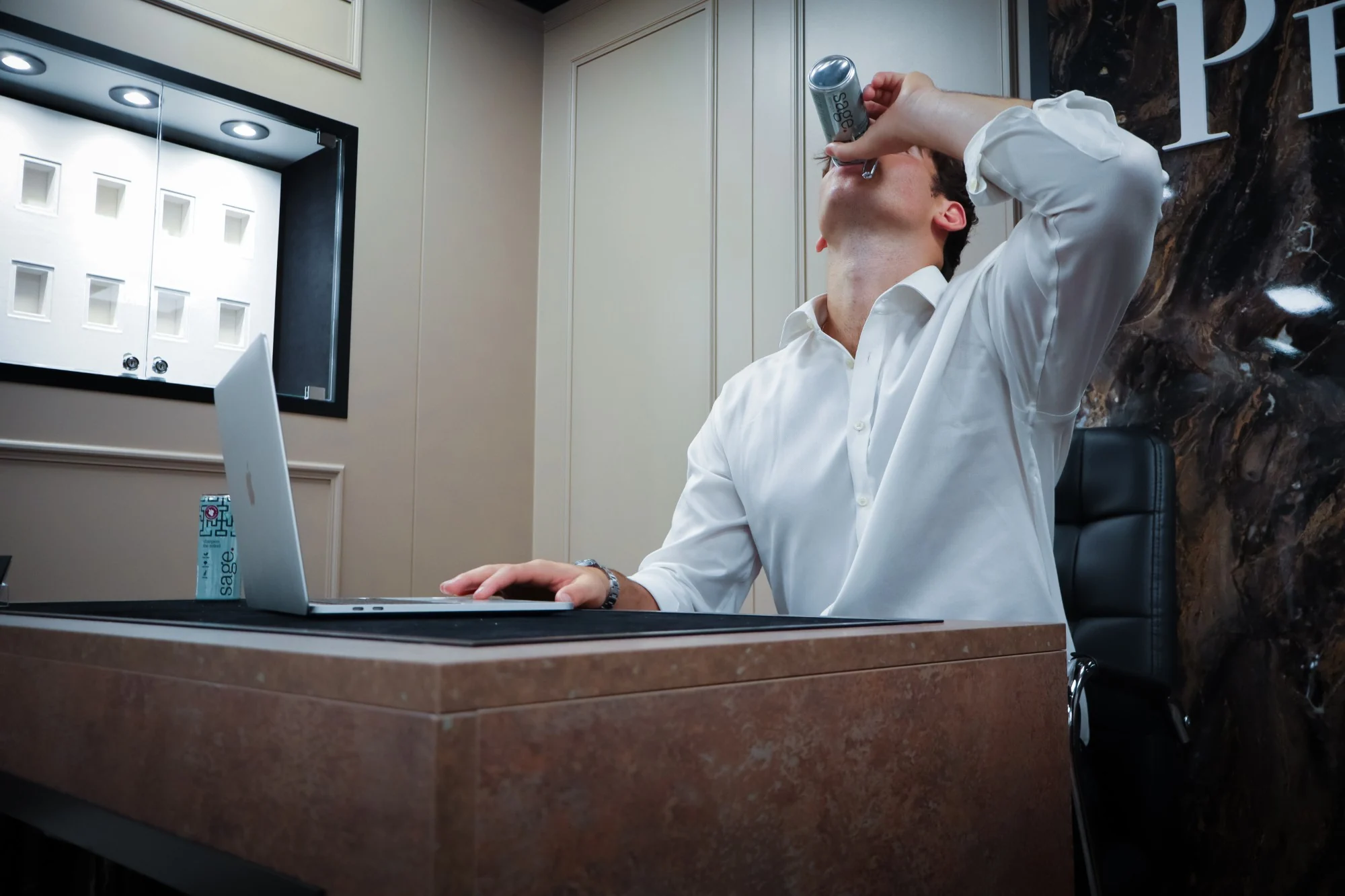 Someone at an office desk drinking a can of sage