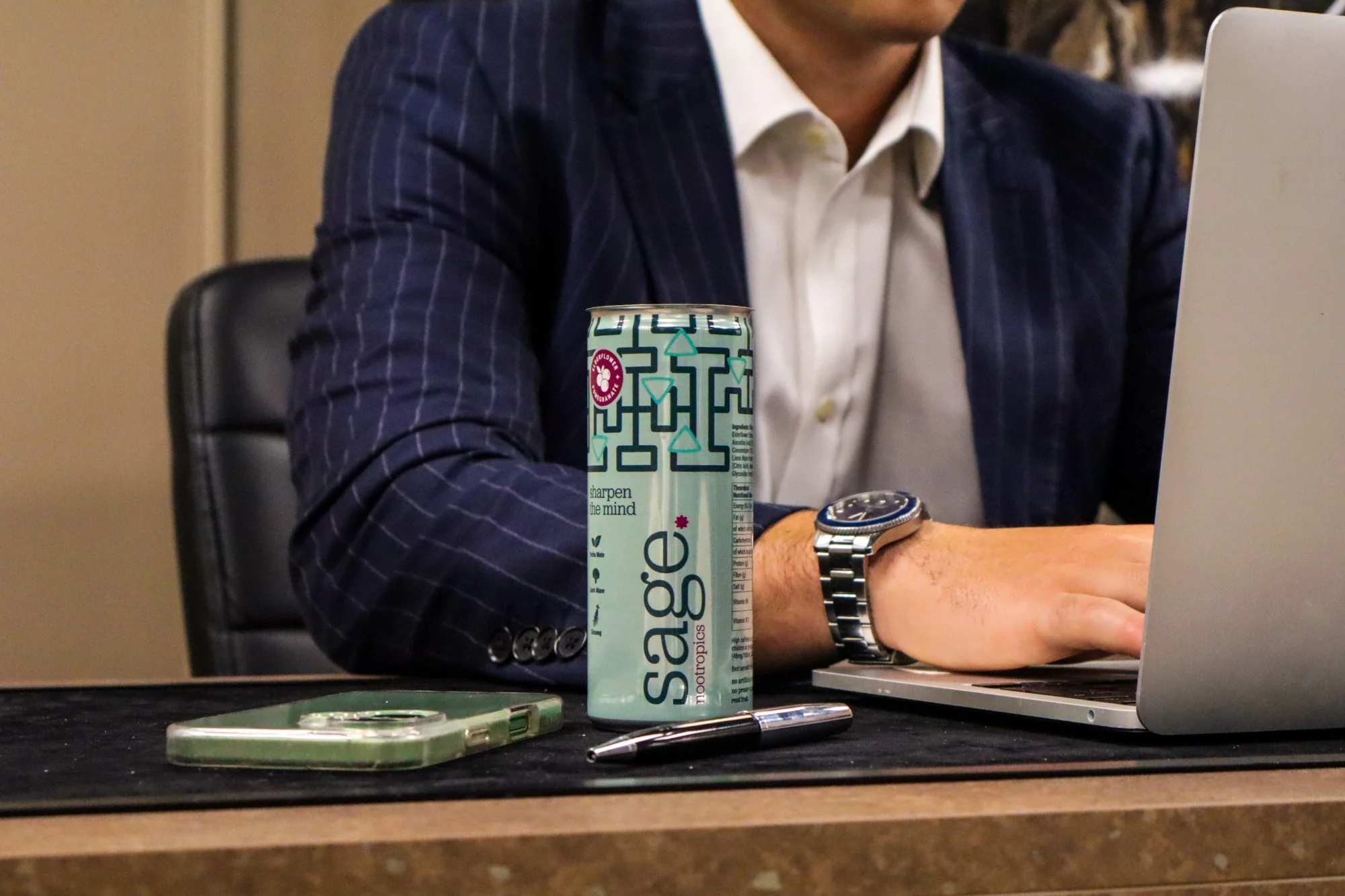 A can of sage on a desk beside someone working at a laptop